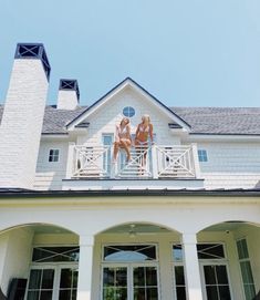 two women in bikinis sitting on the balcony of a large white house with columns