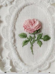 a pink rose is embroidered onto a white doily