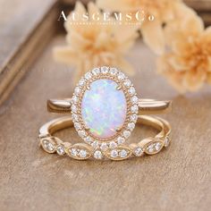 an opal and diamond ring set on a wooden surface with flowers in the background