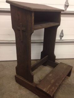 a small wooden table with a cross on it's top and one shelf below