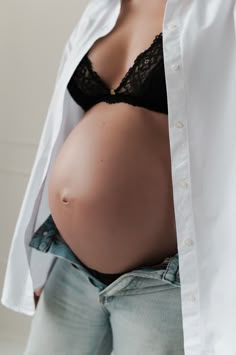 a pregnant woman wearing jeans and a white button up shirt is standing in front of a wall