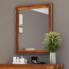 a mirror sitting on top of a wooden dresser next to a vase with flowers in it