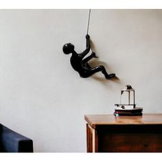 a black figure hanging from the side of a white wall next to a wooden table