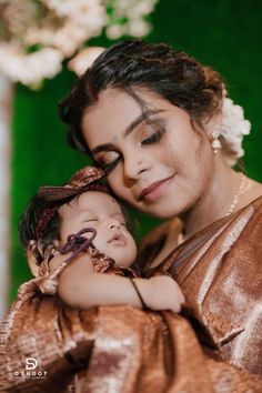 a woman holding a small child in her arms while she is wearing a brown dress