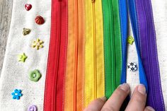 a hand is holding onto some colorful zippers and buttons on a table with other items