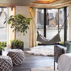 a hammock hanging in the middle of a room with large windows and potted plants