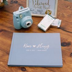 a blue camera sitting on top of a wooden table next to a notepad and photo album