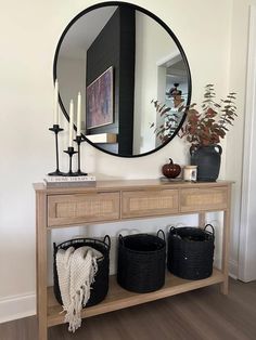 a wooden table with baskets under a round mirror on the wall next to two candles