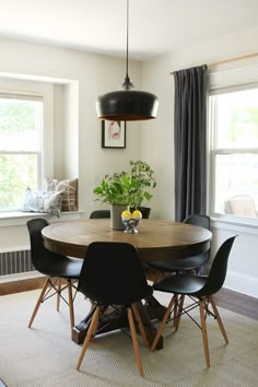 a dining room table with four chairs and a potted plant in the center, next to two windows