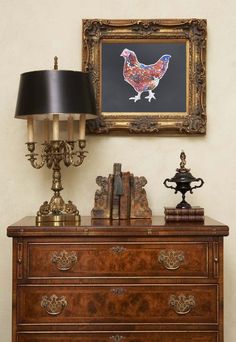 an antique dresser with books, lamp and painting on the wall