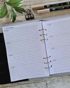 an open planner sitting on top of a wooden table next to a pen and pencil