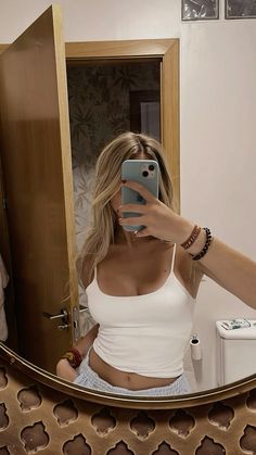 a woman taking a selfie in front of a mirror while wearing a white top