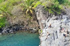 some people are sitting on the rocks by the water and one person is swimming in the river