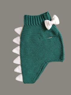 a green knitted dog sweater with white spikes and a bow on the front, made to look like an alligator's tail