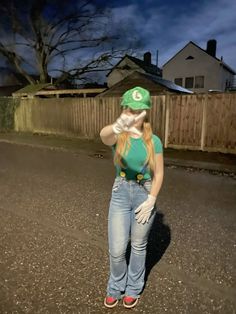 a woman in jeans and a green hat is standing on the street with her hand up to her face