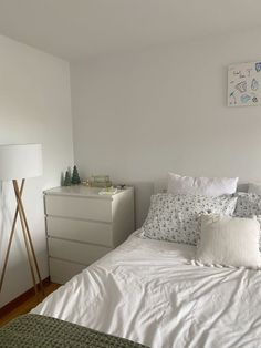 a bed with white sheets and pillows next to a night stand in a small room