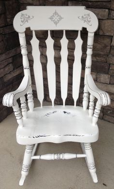 an old white rocking chair sitting in front of a brick wall with the seat up