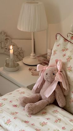 a teddy bear sitting on top of a bed next to a night stand and lamp