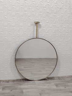 a round mirror sitting on top of a hard wood floor next to a white wall