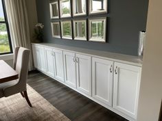 a dining room with white cabinets and chairs in front of a window that has pictures on the wall