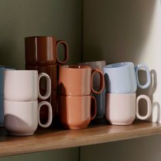 there are many different colored coffee cups on the shelf in front of each other,