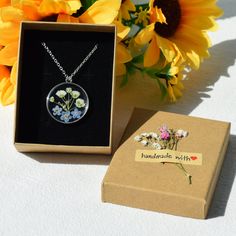 a necklace with flowers in it is sitting next to a box and some sunflowers