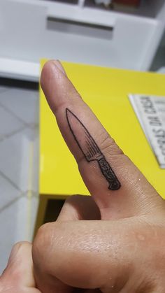 a person's finger with a knife tattoo on it, pointing to the side