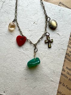 Vintage chic and full of style. Features a 16" antique brass chain with a tumbled green gemstone, vintage plastic heart charm, vintage enamel cross charm, antique brass locket, rough cut citrine gemstone. Let me know if you would like an extension on this necklace at checkout. The necklace will be gift boxed. Bohemian Brass Locket Necklace With Vintage Charm, Vintage Handmade Dangle Charm Necklaces, Handmade Vintage Dangle Charm Necklaces, Spiritual Pendant Charm Necklace With Vintage Charm, Brass Locket Charm Necklaces For Jewelry Making, Spiritual Heart Necklace With Vintage Charm, Bohemian Green Necklaces With Charms, Bohemian Green Necklace With Charms, Spiritual Heart-shaped Necklace With Vintage Charm