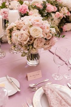 a table set with pink and white flowers in a vase, silverware and place cards