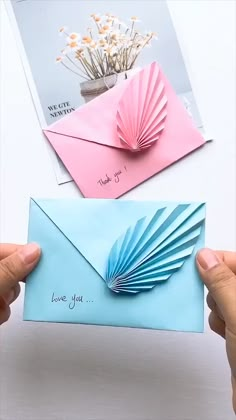 two hands holding up an envelope with folded paper and a flower in the corner on top