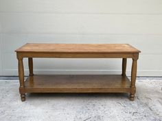 a small wooden table sitting on top of a cement floor next to a white wall