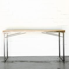 a wooden table with metal legs against a white brick wall