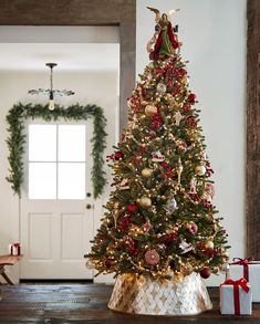 a decorated christmas tree stands in front of a white door with red and gold ornaments