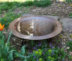 a metal bowl sitting on top of a grass covered ground next to purple and yellow flowers