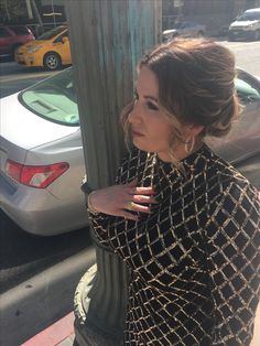 a woman leaning against a pole on the sidewalk