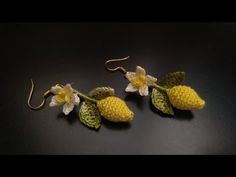 three crocheted lemons with leaves and flowers hanging from hooks on a black surface