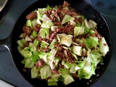 a skillet filled with lettuce and meat on top of a gas stove