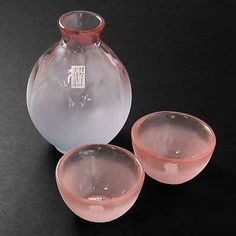 two pink glass bowls and a vase on a black table top, with one bowl in the foreground