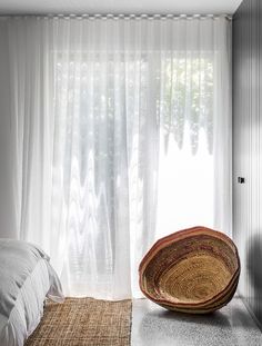 a bed sitting next to a window with sheer curtains on the windowsill in front of it