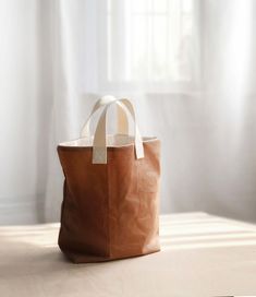 a brown leather bag sitting on top of a table next to a window with white curtains