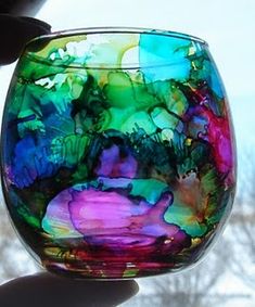 a hand holding a colorful glass bowl in front of a window