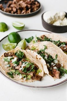 three tacos on a plate with limes and other ingredients