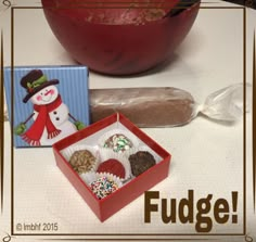 a red bowl filled with assorted candy next to a box of fudges