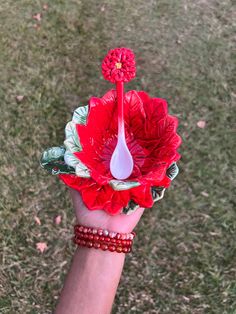 a woman's hand holding a red flower in the grass