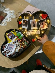 a heart shaped box filled with photos and magnets on top of a wooden table