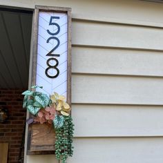 a house number sign hanging from the side of a building next to a planter