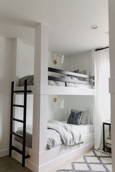 there are bunk beds in this room with white walls and wood flooring, along with black ladders