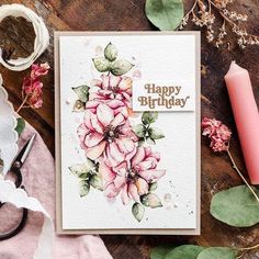 a birthday card with pink flowers on it next to some candles and other things around