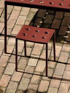 a red bench sitting on top of a brick road next to a small table with holes in it