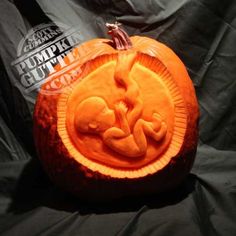 an orange carved pumpkin sitting on top of a black cloth covered bed next to a bottle